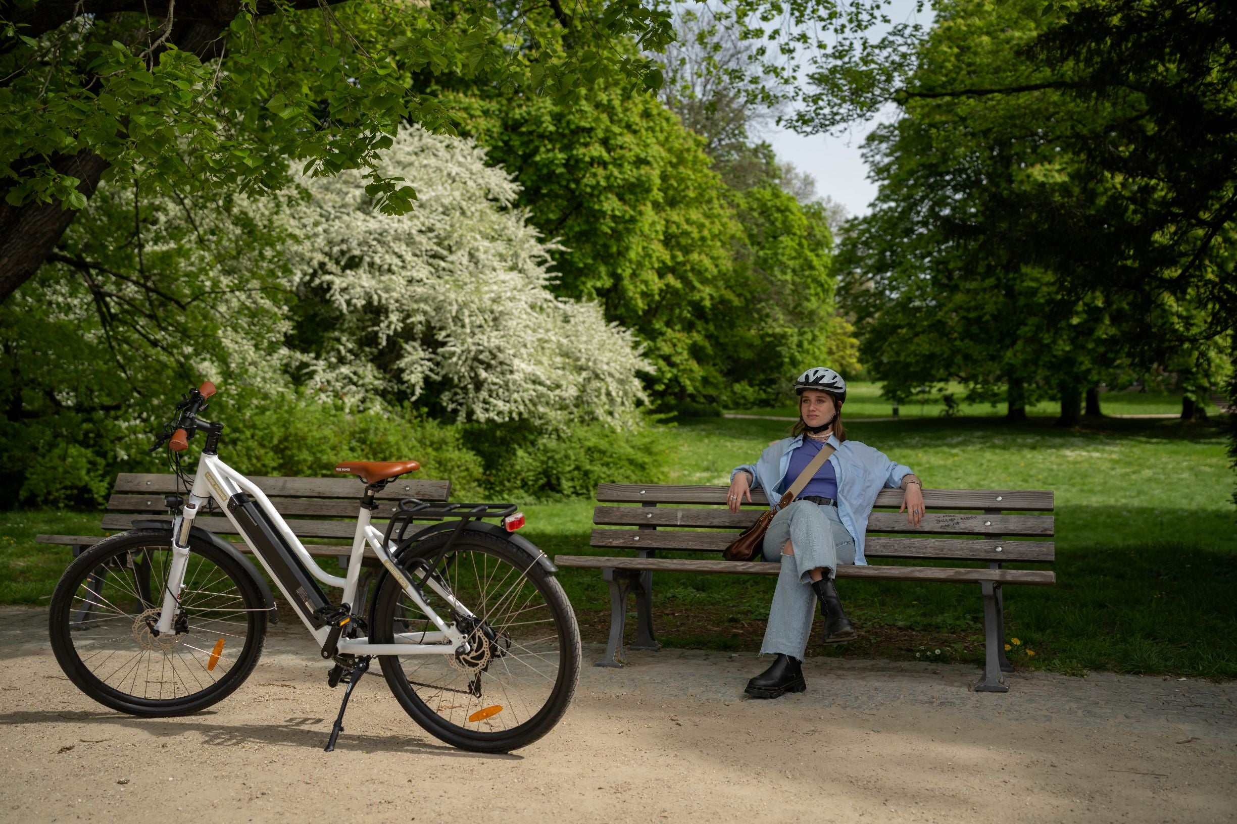 A woman sat on a bench, with an e-bike parked in front of her.